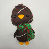 Plush penguin resembling chocolate cake with white icing and red and green sprinkles and a red and green scarf on a white background