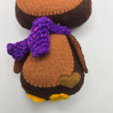 Close-up of a plush Chocolate Penguin with brown body, purple scarf, and light brown heart on a white background