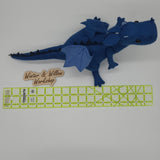 Handmade blue felt dragon plush with black button eyes, dark felt back spikes, and a stitched light blue belly. The soft dragon stands with a curved tail and small wings.