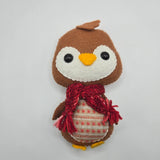 Small plush Gingerbread Penguin with a red scarf and stomach with red ball patterns and white line patterns on it on a light gray background