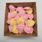 Pink and yellow felt heart-shaped ravioli in a brown box on a light gray background