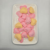 Pink and yellow heart-shaped ravioli on a white plate against a gray background