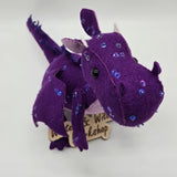 Handmade purple felt dragon plush with a light lavender belly, small white horns, and black button eyes. The dragon is decorated with shimmering sequins across its head, wings, and body.