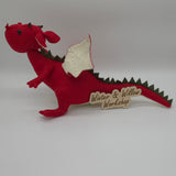 Handmade red felt dragon plush with white wings, small horns, and black button eyes. The soft stuffed dragon stands upright with a curved tail and stitched details.