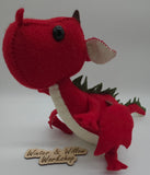 Handmade red felt dragon plush with white wings, small horns, and black button eyes. The soft stuffed dragon stands upright with a curved tail and stitched details.