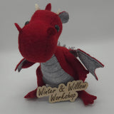 Handmade red felt dragon plush with gray wings, small white horns, and black button eyes. The soft dragon has a stitched gray belly and stands upright with outstretched wings.