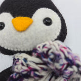 Close-up of a penguin plush face with a multicolored scarf on a white background.