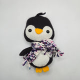 Penguin plush with a multicolored black, purple, blue, pink, white scarf on a light gray background