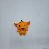 Handmade pumpkin gremlin felt plush with an orange pumpkin body, pointy ears, and stitched pumpkin lines. The character has one black button eye, a winking stitched eye, and a playful tongue sticking out with a small green leaf and stem on top.