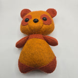Small plush toy resembling a bear with a brown color scheme on a light gray background
