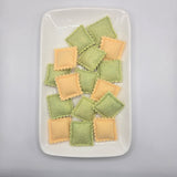 Green and yellow ravioli on a white plate against a gray background