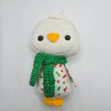 Small white penguin with a green scarf on a light gray background.